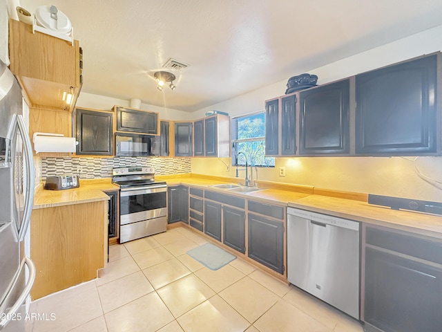 kitchen featuring sink, backsplash, light tile patterned floors, and appliances with stainless steel finishes