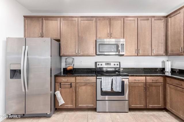 kitchen with dark stone countertops, light tile patterned floors, and stainless steel appliances