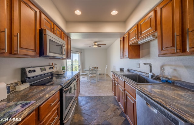 kitchen with appliances with stainless steel finishes, sink, dark stone countertops, and ceiling fan