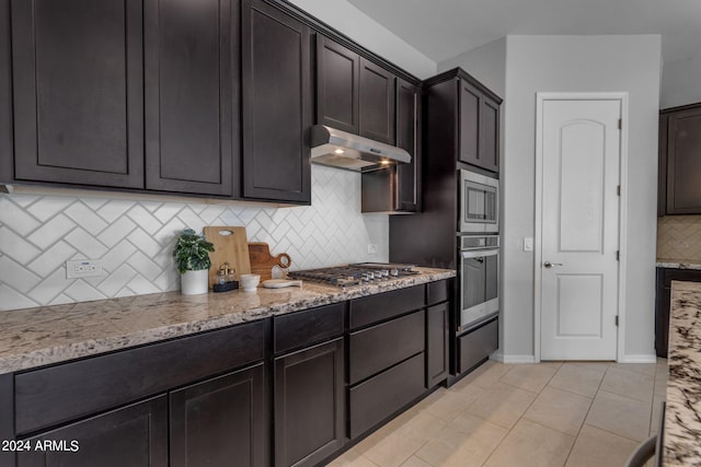 kitchen featuring dark brown cabinetry, light stone counters, light tile patterned floors, and appliances with stainless steel finishes