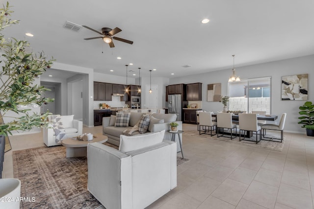 tiled living room with ceiling fan with notable chandelier