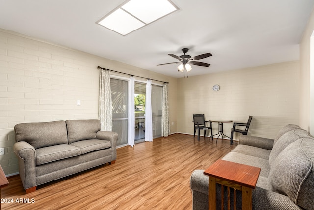 living room featuring light wood-type flooring, ceiling fan, and brick wall