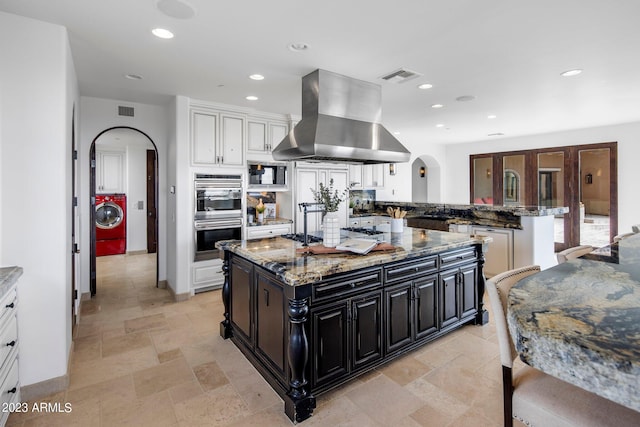 kitchen with a center island, washer / dryer, island exhaust hood, and stone counters