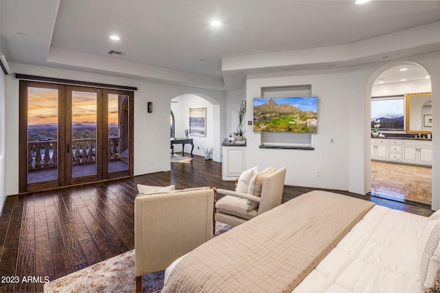 bedroom featuring access to exterior, dark hardwood / wood-style floors, a raised ceiling, and ensuite bathroom