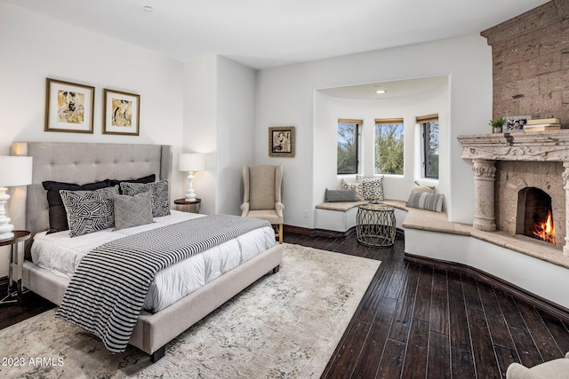 bedroom with a stone fireplace and dark hardwood / wood-style flooring