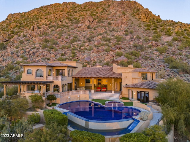 rear view of property with a mountain view, a swimming pool with hot tub, a balcony, and a patio