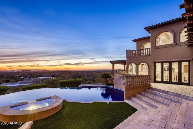 pool at dusk with a patio area and an in ground hot tub