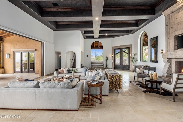 living room with coffered ceiling, french doors, a towering ceiling, a fireplace, and beam ceiling