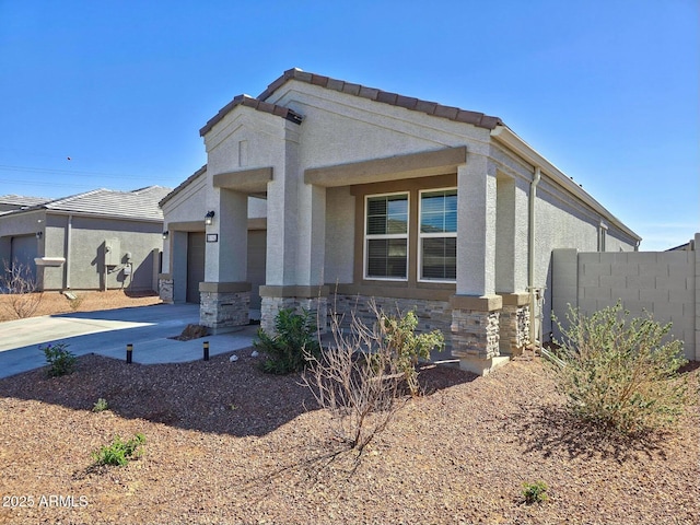 view of front of house with driveway, a garage, stone siding, fence, and stucco siding