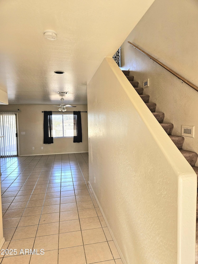 corridor with visible vents, baseboards, stairway, light tile patterned floors, and a textured wall