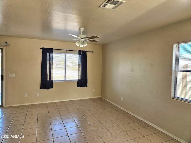 empty room featuring visible vents, a ceiling fan, a textured ceiling, light tile patterned flooring, and baseboards