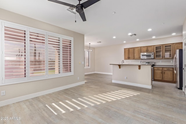 kitchen featuring stainless steel appliances, visible vents, baseboards, brown cabinetry, and a kitchen bar