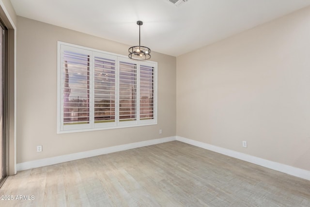 unfurnished room featuring a chandelier, light wood finished floors, and baseboards