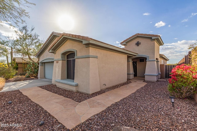 view of side of home with a garage, concrete driveway, a tile roof, fence, and stucco siding