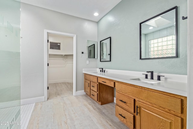 bathroom featuring double vanity, a spacious closet, baseboards, and a sink