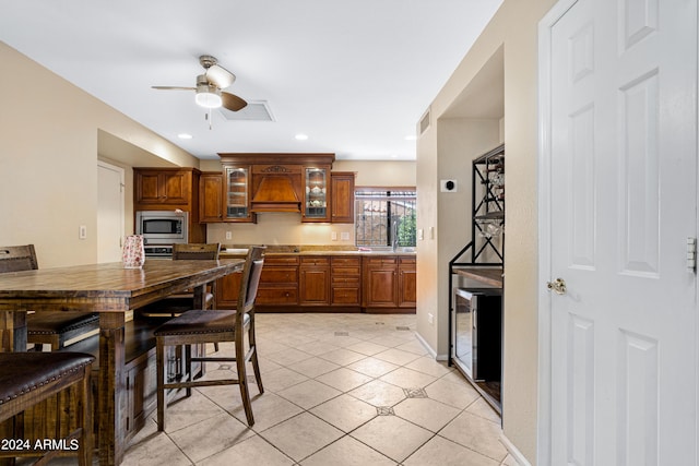 kitchen with ceiling fan, stainless steel microwave, custom exhaust hood, and light tile patterned floors