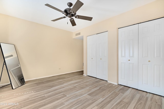 unfurnished bedroom featuring ceiling fan, light hardwood / wood-style floors, and multiple closets