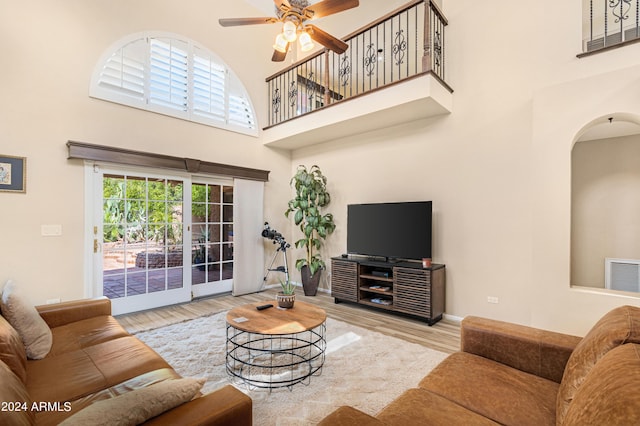 living room featuring ceiling fan, light hardwood / wood-style floors, and a towering ceiling