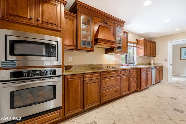 kitchen featuring appliances with stainless steel finishes, sink, custom exhaust hood, light tile patterned floors, and light stone countertops