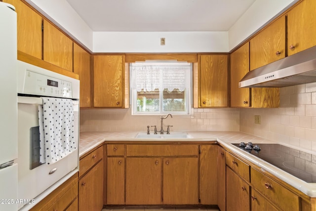 kitchen with black electric stovetop, tile counters, under cabinet range hood, and a sink