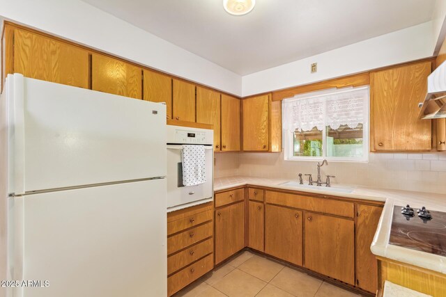 kitchen with light countertops, backsplash, a sink, light tile patterned floors, and white appliances