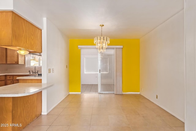 unfurnished dining area featuring light tile patterned flooring, baseboards, a sink, and an inviting chandelier