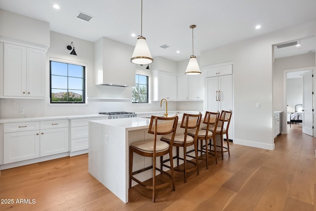 kitchen featuring light wood-style floors, wall chimney exhaust hood, white cabinets, and light countertops