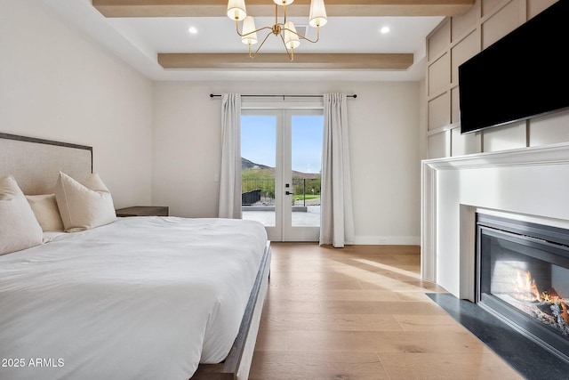 bedroom featuring a chandelier, a fireplace with flush hearth, french doors, light wood-style floors, and access to outside