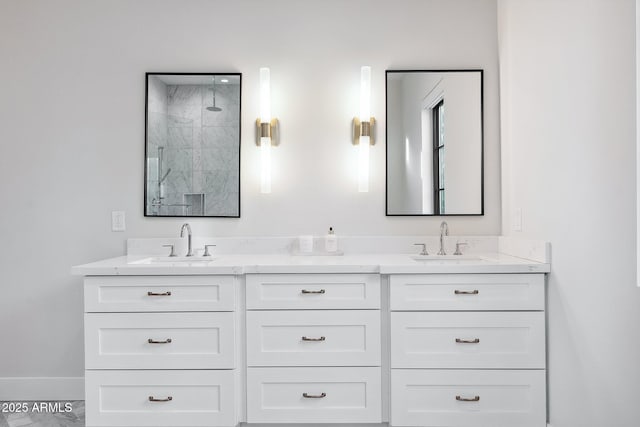 bathroom with a sink, a marble finish shower, baseboards, and double vanity