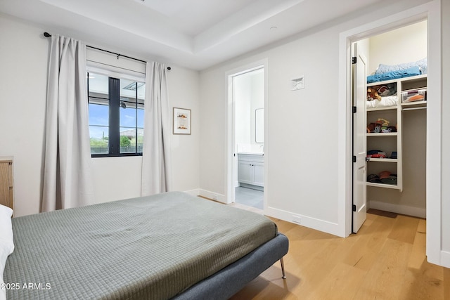 bedroom featuring a walk in closet, baseboards, light wood-type flooring, ensuite bathroom, and a closet