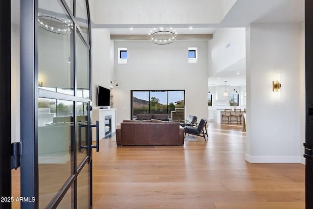 living room featuring visible vents, baseboards, an inviting chandelier, light wood-style floors, and a towering ceiling