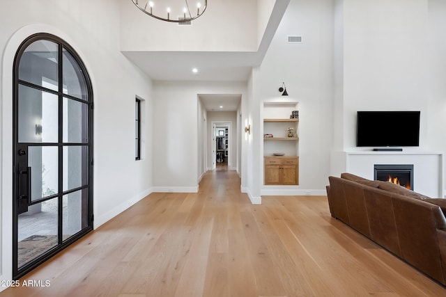 foyer with light wood finished floors, a warm lit fireplace, and a towering ceiling