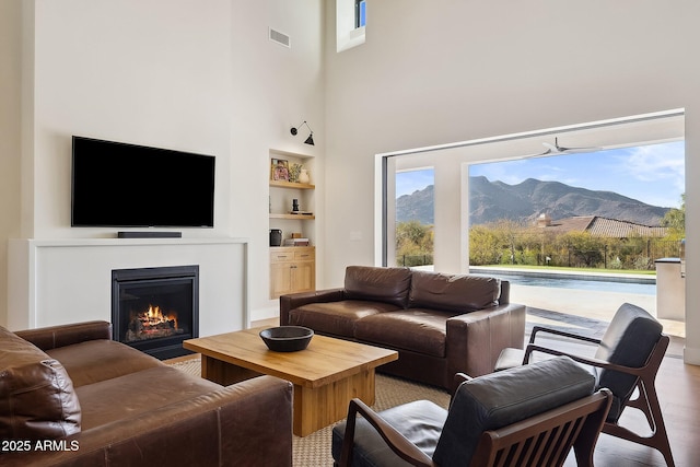 living area featuring visible vents, built in shelves, a fireplace with flush hearth, wood finished floors, and a towering ceiling