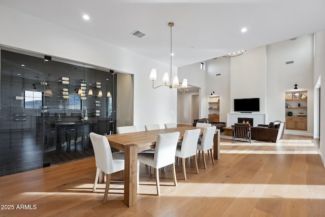 dining space featuring visible vents, an inviting chandelier, light wood-style flooring, and a towering ceiling