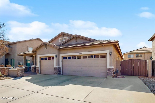 view of front of house with driveway, stone siding, an attached garage, and a gate