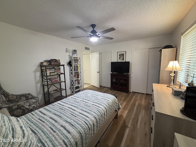 bedroom featuring dark hardwood / wood-style flooring, ceiling fan, two closets, and a textured ceiling