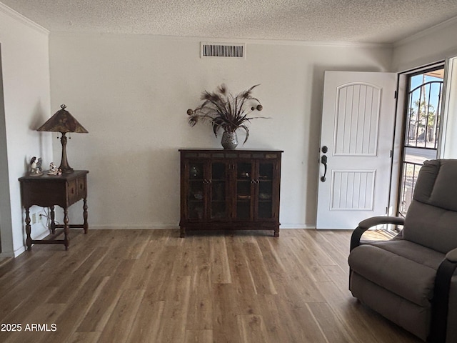 sitting room featuring crown molding, wood-type flooring, and a textured ceiling