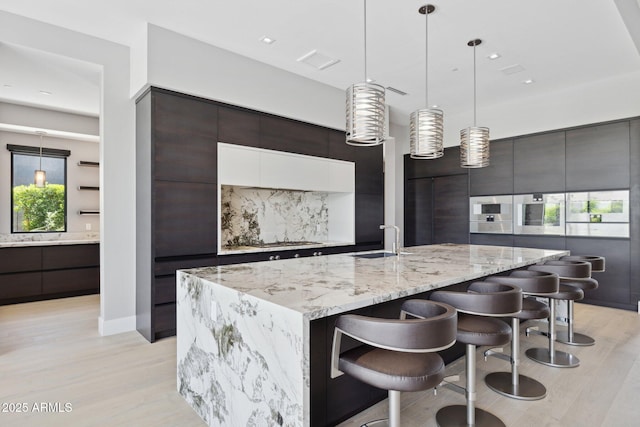6908 E Cactus Wren Rd, Paradise Valley, AZ 85253 - kitchen with modern cabinets, light wood-style flooring, light stone countertops, pendant lighting, and a kitchen bar