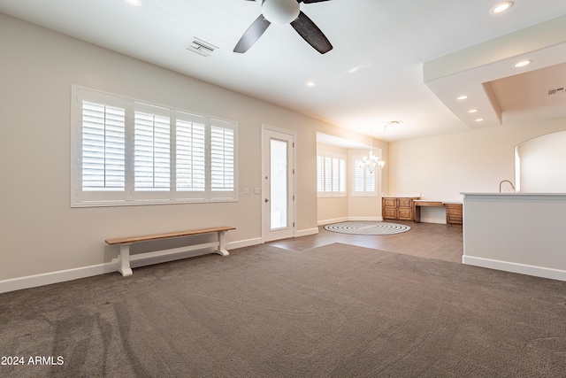 unfurnished living room featuring dark colored carpet and ceiling fan with notable chandelier