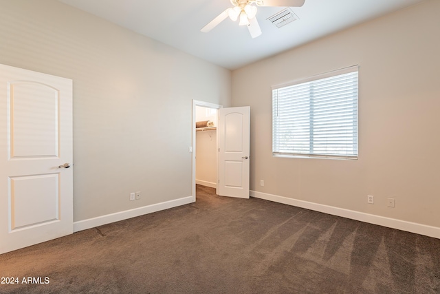 unfurnished bedroom with dark colored carpet, ceiling fan, and a walk in closet