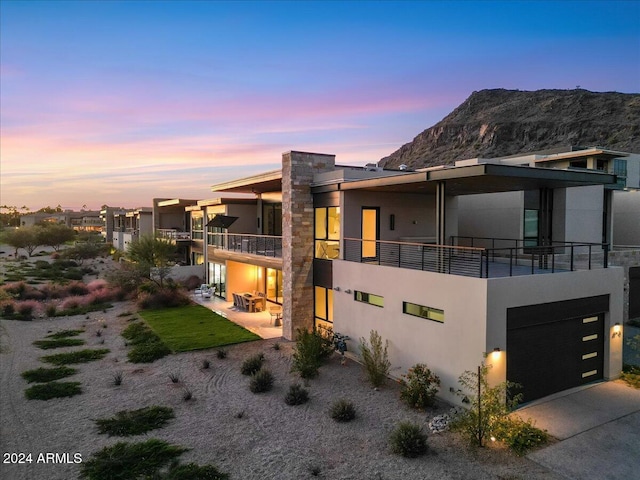 back of house at dusk with a balcony, stucco siding, a mountain view, and concrete driveway