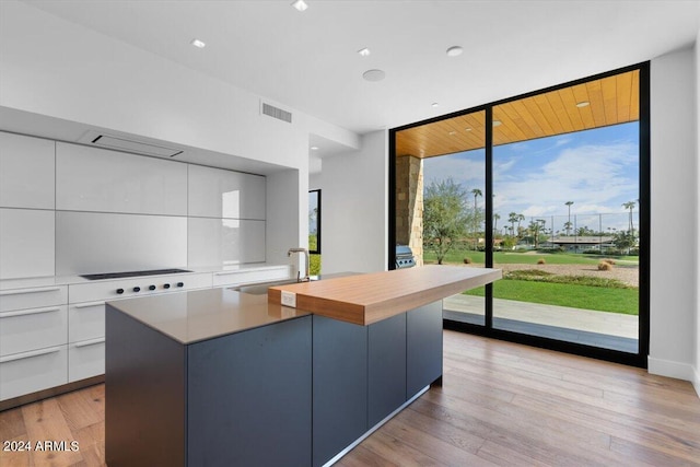 kitchen with floor to ceiling windows, a kitchen island, sink, light hardwood / wood-style flooring, and white cabinetry