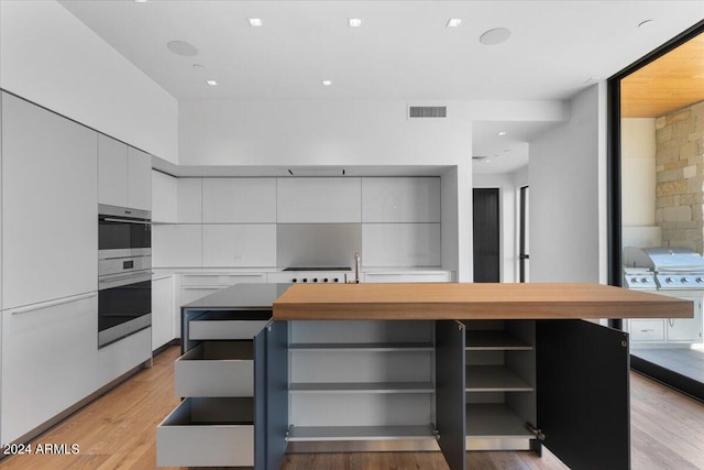 kitchen with double oven, a kitchen island, white cabinets, and light wood-type flooring