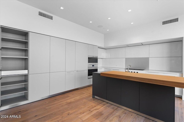 kitchen featuring a large island, stainless steel double oven, cooktop, white cabinets, and light wood-type flooring