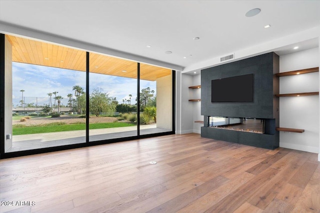 unfurnished living room with light wood-type flooring, a large fireplace, and floor to ceiling windows