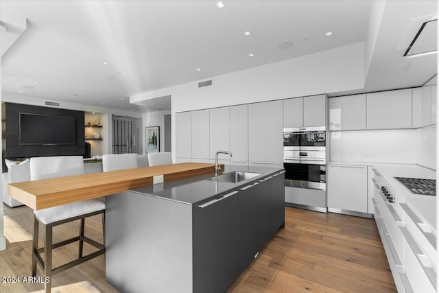 kitchen featuring double oven, sink, white cabinets, light hardwood / wood-style floors, and an island with sink