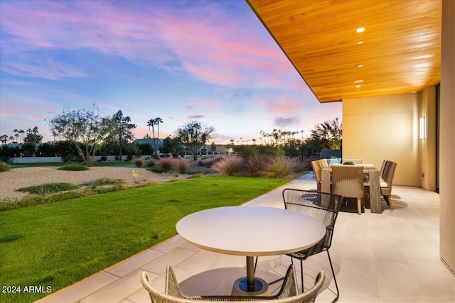 patio terrace at dusk featuring a lawn