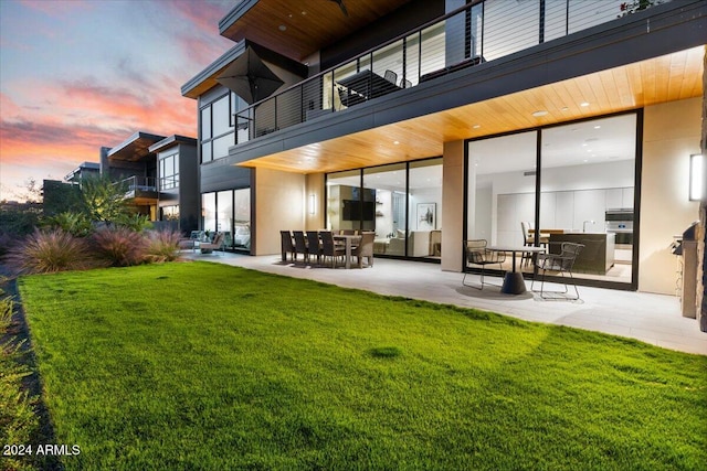 back house at dusk featuring a patio area, a balcony, and a yard