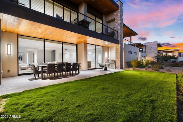 back house at dusk with a yard, a patio, and a balcony