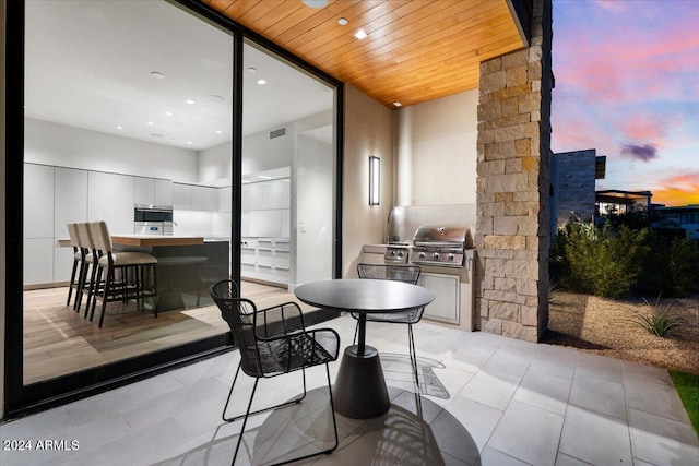 patio terrace at dusk featuring area for grilling, a grill, and a bar